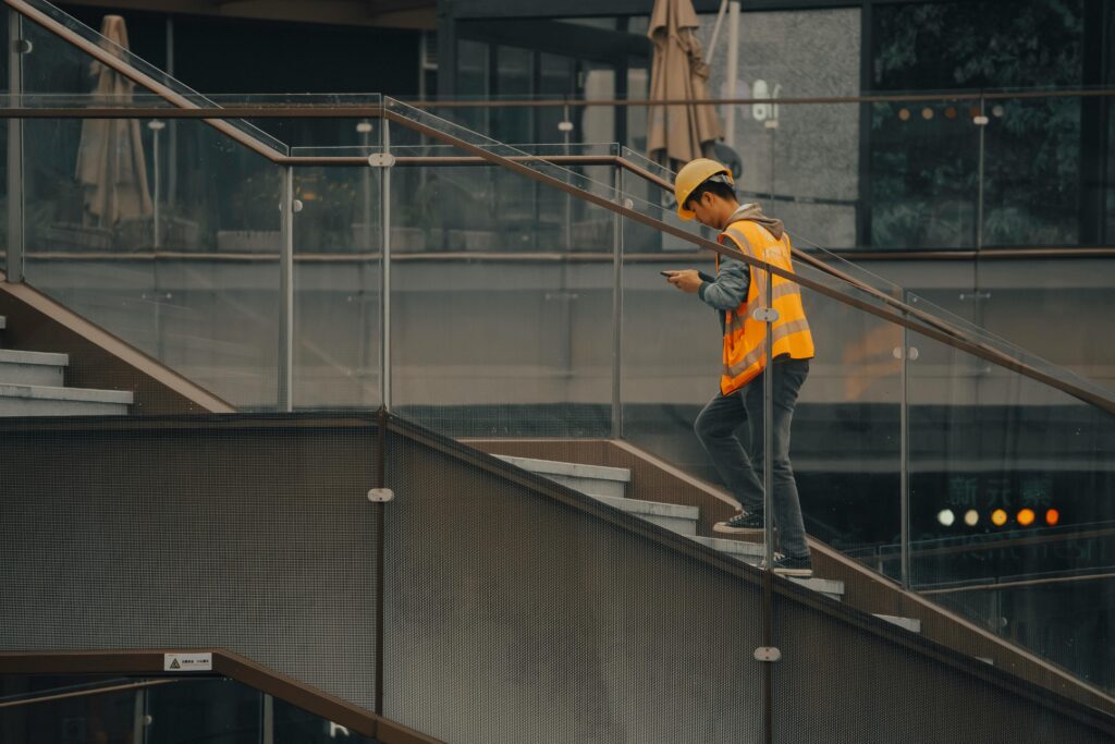 An adult construction worker in a hard hat and vest ascending stairs inside a building.
